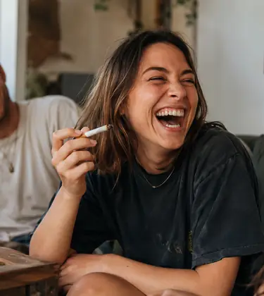 Friends laughing together in a cozy living room during a relaxed cannabis session.