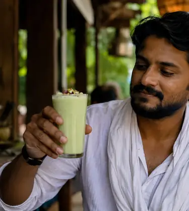 A man at an Indian market stall holds a glass of pale green bhang lassi.