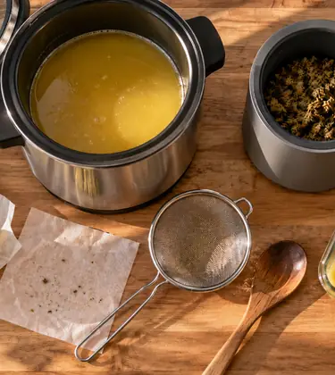 An herbal infuser full of cannabis butter beside a decarboxylator with toasted ground cannabis on an oak kitchen island